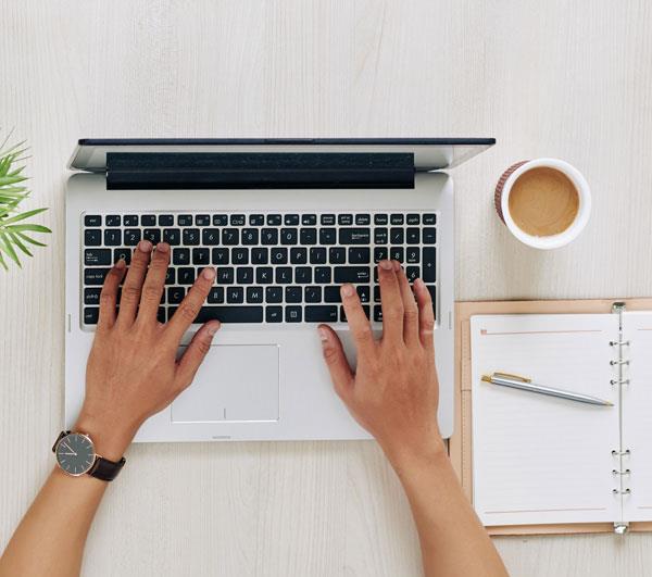 Photo image of a person's hands typing on a laptop.