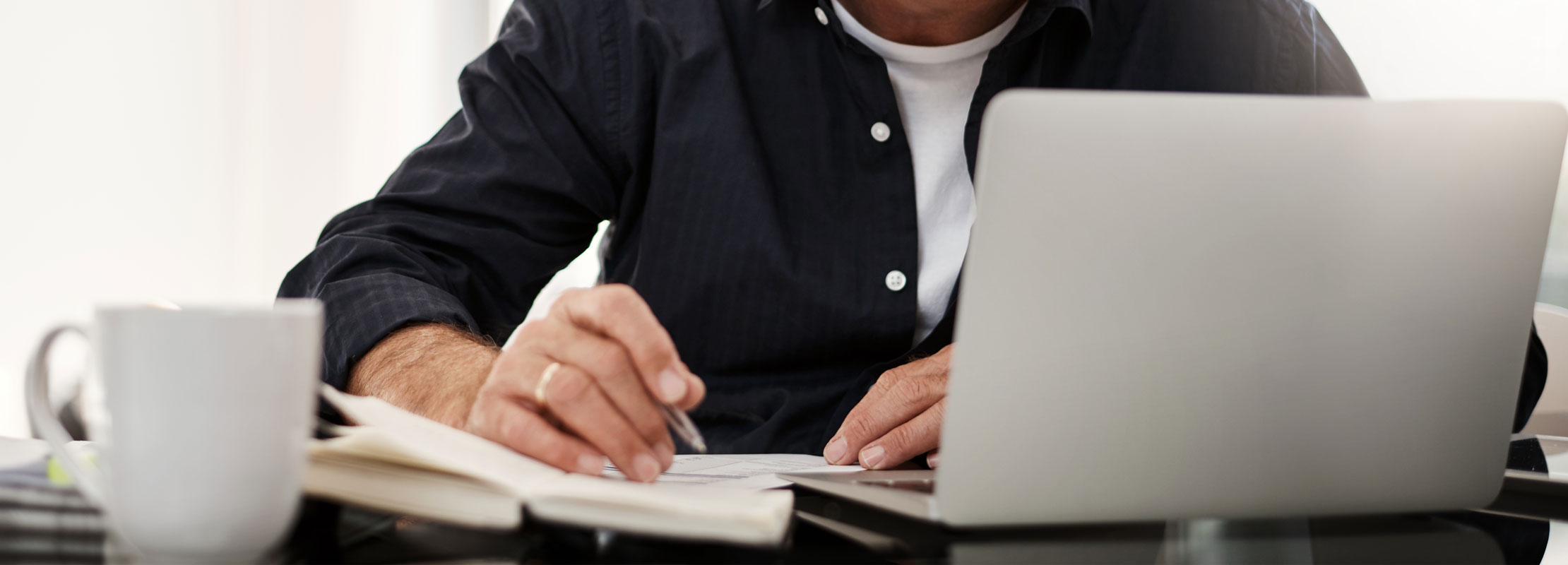 Photo image of person sitting at a desk with a laptop and notebook taking notes.